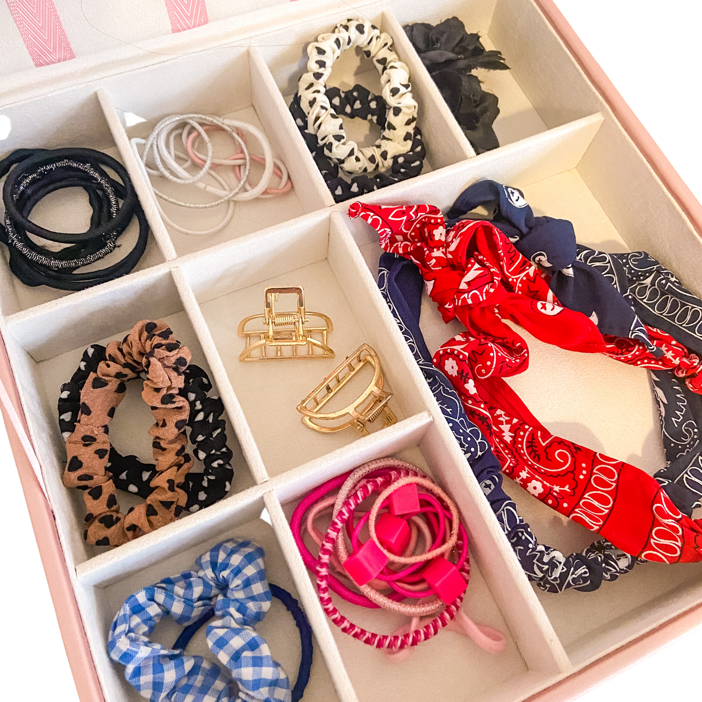 The image shows the internal of bottom section of the pink hair accessory organiser. The grid inside has one large compartment for hair bands and larger accessories, and there are 8 smaller sections to hold hair bobbles and scrunchies.