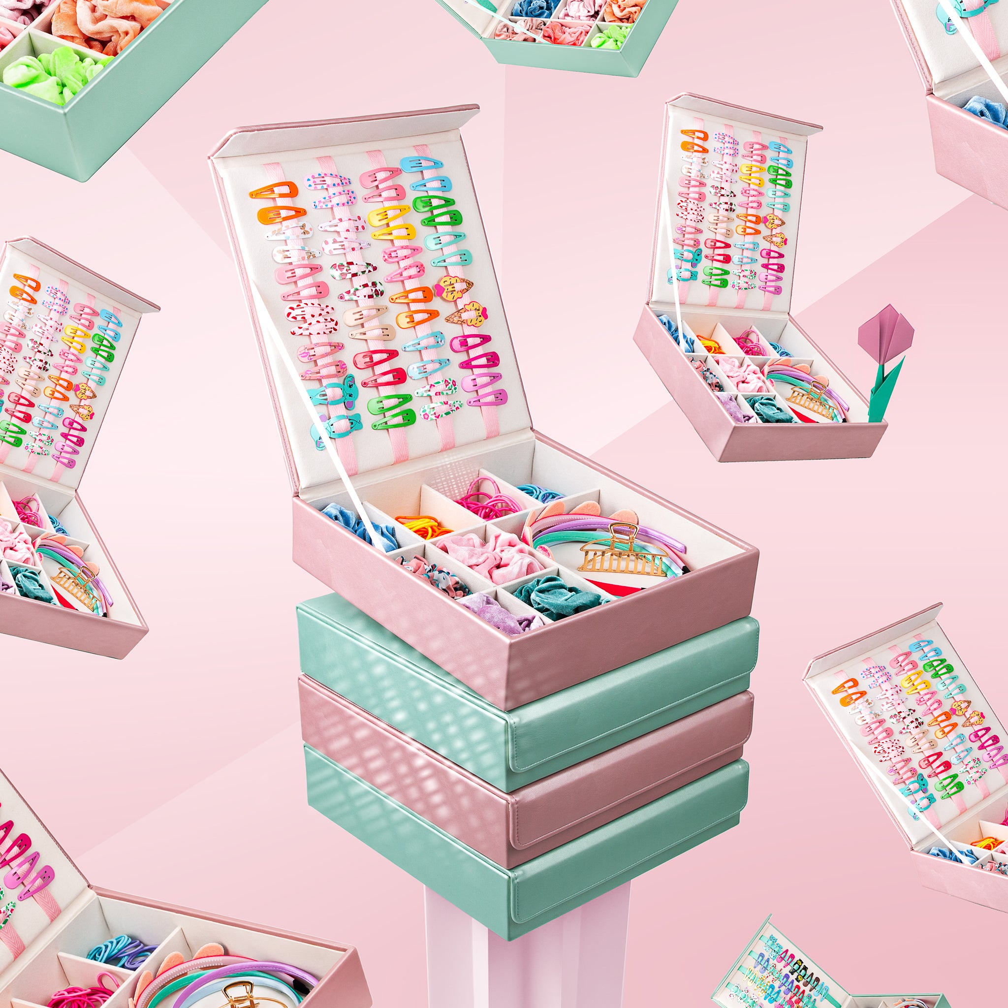 Fun image showing the mint green and pink hair accessory storage boxes stacked on top of one another, and surrounded by floating images. The background is pink