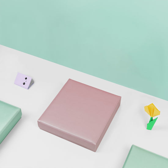 In this stop motion image the Pink hair accessory organiser is filled with hair accessories and is placed open on a white surface with a mint green backdrop. It is accessorised with some origami flowers and two mint green hair accessory organisers are visible in the photograph. The box opens and closes several times and the scrunchies magically move out of the box and then back in.