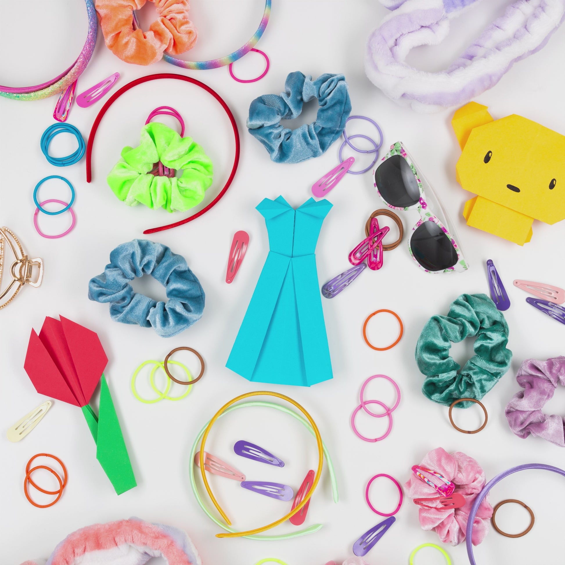 This stop motion image shows lots of hair accessories against a white background. The accessories wiggle out of the frame as the mint green hair accessory storage box enters. A finger presses on it and it turns to pink. It then opens and it is empty. With the wave of a hand it is filled with beautiful hair accessories. The box then closes and wiggles out of the frame